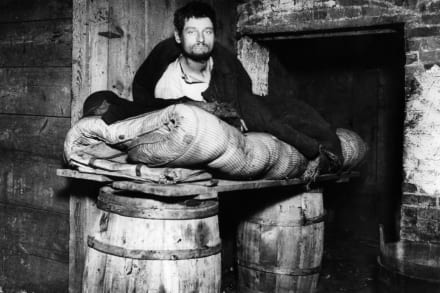 En mand på sin seng stablet op på tønder i en kælder i New York omkring 1890. Fotografien Jacob A. Riis er blevet hyldet for at afsløre arbejderklassens kummerlige vilkår, men Susan Sontag afviser fotografiet som et middel til revolution eller empati.